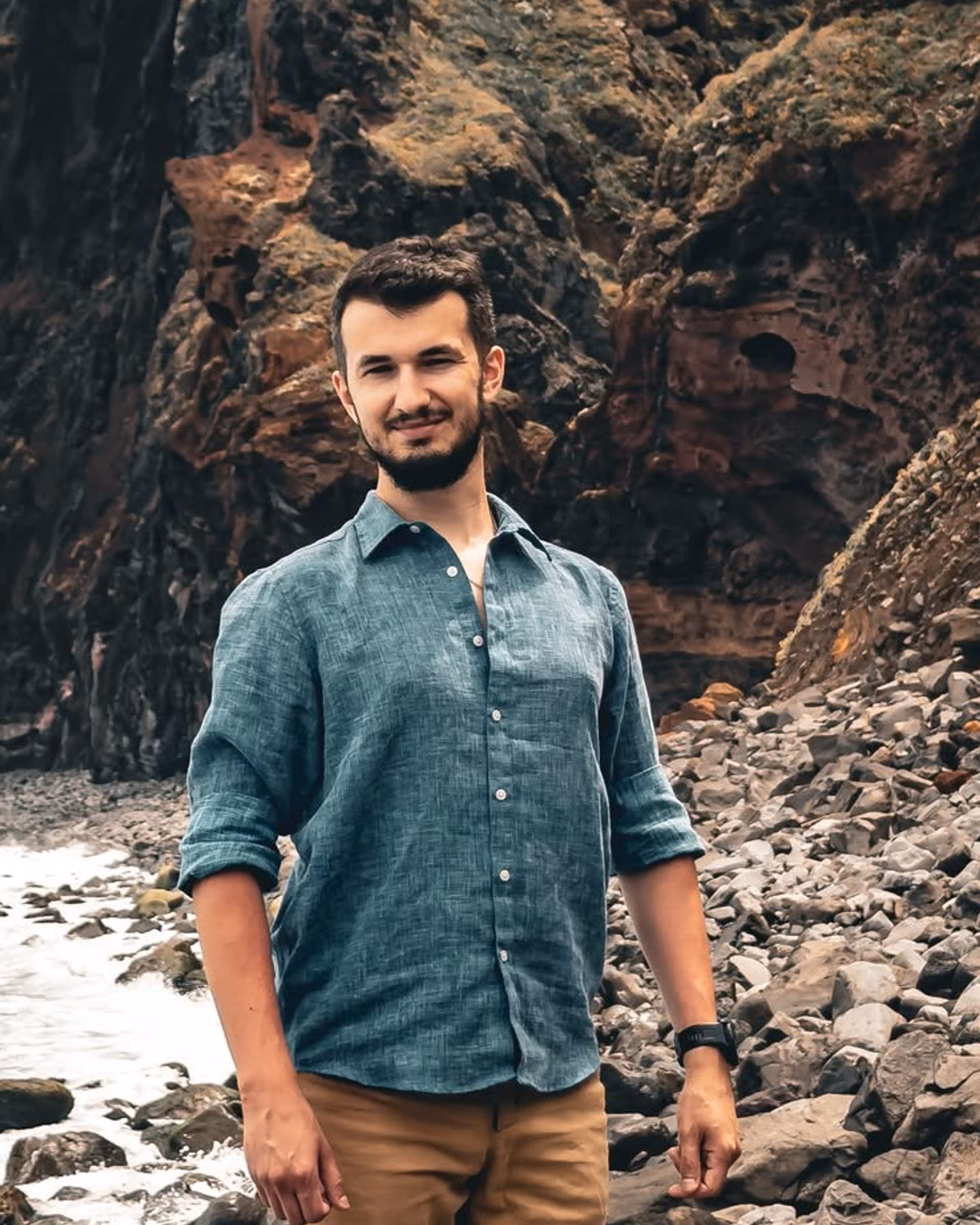 Rafał in a blue shirt on a rocky beach beneath steep coastal cliffs